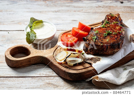 Grilled steak on a cutting board. Appetizing roasted meat with vegetables and herbs. Copy space. Close-up Grilled steak on a cutting board. Appetizing roasted meat with vegetables and herbs. Copy space. Close-up 88464771