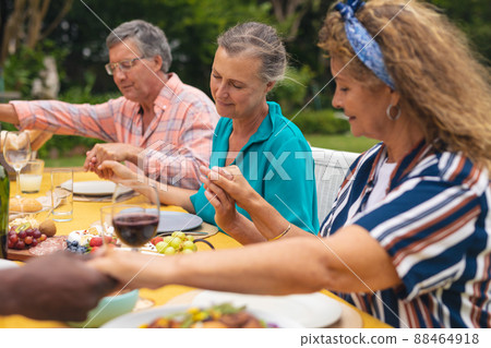 Multiracial senior male and female friends holding hands and praying at table in backyard Multiracial senior male and female friends holding hands and praying at table in backyard 88464918