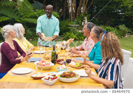 African american senior man serving food to caucasian friends at table in backyard African american senior man serving food to caucasian friends at table in backyard 88464970