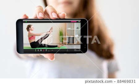 Fitness online. Virtual gym. Home workout. Girl hand showing athletic woman performing stretching exercise on smartphone screen isolated on light blur background. 88469831