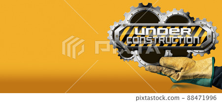 Gloved Hand Holding an Under Construction Sign on Orange Background 88471996