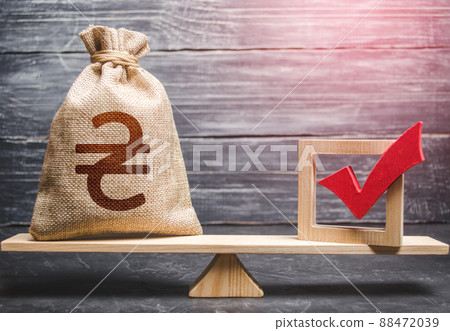 Red vote tick and a ukrainian hryvnia money bag on scales. Estimating cost of making a decision and consequences in the future. Corruption risks. Concept of lobbying for decisions and laws. 88472039