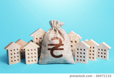 Ukrainian hryvnia money bag among town houses figurines. Municipal budgeting. Rental business. Realtor services. Sale of real estate. property taxes. Tax collection, investment in city development. 88472110