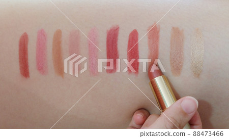 Colorful lipstick strokes in different shades of red, drawn onto human skin. With a hand holding a lipstick, drawing a stroke. Colorful lipstick strokes in different shades of red, drawn onto human skin. With a hand holding a lipstick, drawing a stroke. 88473466