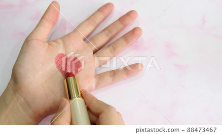 Hand holding a tube of lipstick, drawing a heart shape in the center of a palm. Hand holding a tube of lipstick, drawing a heart shape in the center of a palm. 88473467