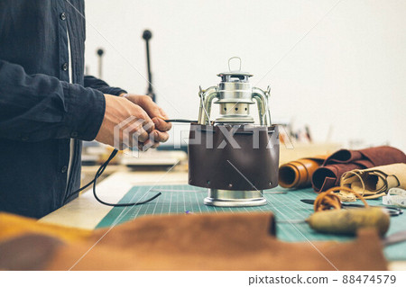 Male tanner working makes a leather case for a camping kerosene lamp. 88474579