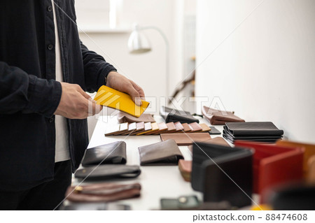 Craftsman hands laying out leatherwork on wooden showcase at leather workshop. Handwork accessories 88474608