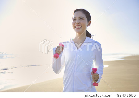 A young woman in sportswear walking on a sandy beach 88475699