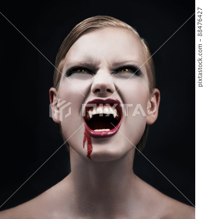 Filled with bloodlust. A provocative female vampire with blood running down her chin. 88476427
