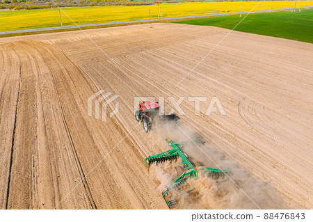 Aerial View. Tractor Plowing Field. Beginning Of Agricultural Spring Season. Cultivator Pulled By A Tractor In Countryside Rural Field Landscape. Dust Rises From Under Plows 88476843