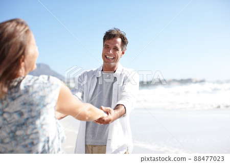 They bring each other so much joy. A happy mature couple holding hands while facing each other on the beach. They bring each other so much joy. A happy mature couple holding hands while facing each other on the beach. 88477023