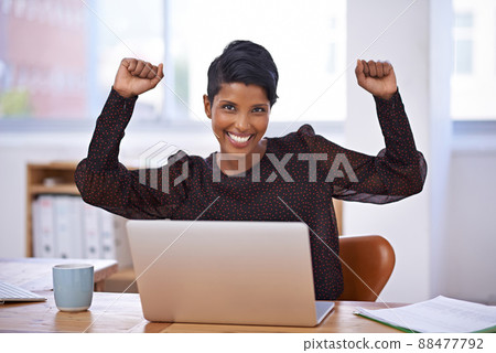 Her business is reaching new heights. A portrait of a beautiful young woman sitting in her office and raising her arms enthusiastically. 88477792