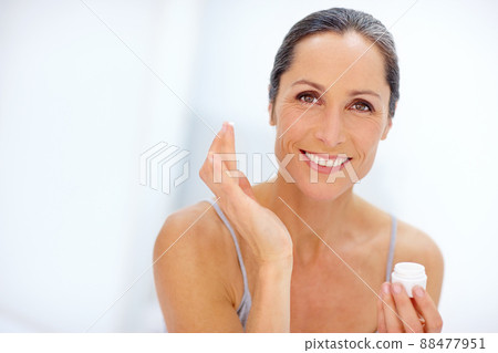 Adding a touch of moisture. Shot of an attractive mature woman applying moisturizer to her skin. 88477951