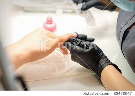 Close up professional manicure master holds the female hand of the customer and disinfects nails in a nail salon 88478047