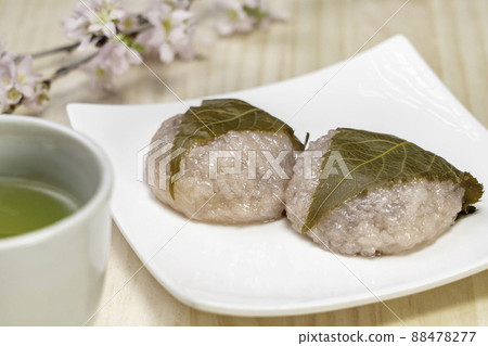 Sakura mochi, cherry blossoms and green tea on a white plate with a wood grain background 88478277