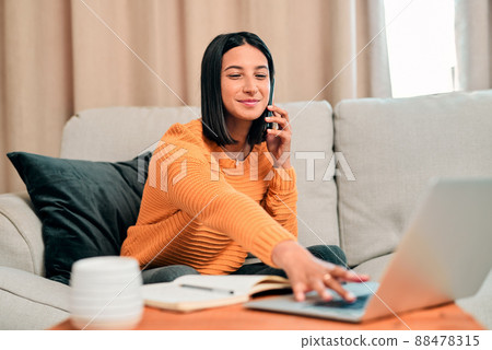 Lifes short, spend it productively. Shot of a young woman using a laptop and smartphone while working on the sofa at home. 88478315