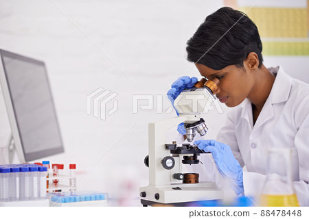 A perfectionist at work. A young scientist using a microscope at her desk in her lab. 88478448