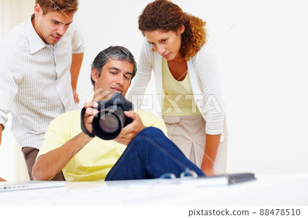 Photographers looking at pictures in camera. Male photographer showing pictures to his colleagues in his camera. 88478510