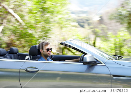 He loves his convertible. A young male driving a silver convertable. 88479223