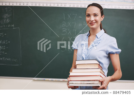 Getting ready for todays lesson. A pretty teacher holding a stack of books in her classroom. Getting ready for todays lesson. A pretty teacher holding a stack of books in her classroom. 88479405