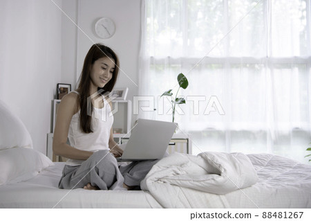 Beautiful Asian woman in pyjamas using laptop sitting on the bed in the house. Beautiful Asian woman in pyjamas using laptop sitting on the bed in the house. 88481267