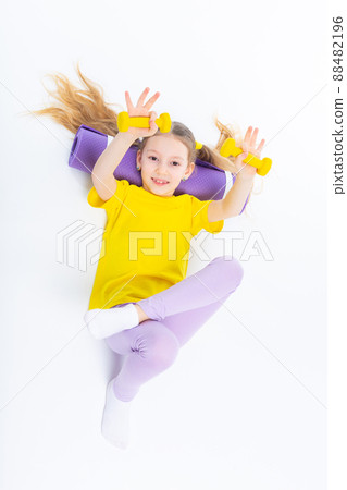 Little cute happy girl lies with dumbbells and gymnastic mat. Isolated on white background. View from above. Little cute happy girl lies with dumbbells and gymnastic mat. Isolated on white background. View from above. 88482196