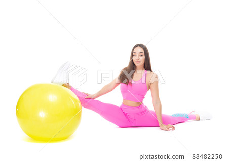A beautiful, athletic, slim, smiling and cheerful woman in a pink tracksuit demonstrates stretching. Sits on a twine supported by a yellow fitball. Pilates. Lifestyle concept with sports and gym A beautiful, athletic, slim, smiling and cheerful woman in a pink tracksuit demonstrates stretching. Sits on a twine supported by a yellow fitball. Pilates. Lifestyle concept with sports and gym 88482250