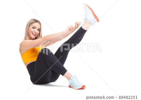 A beautiful, athletic, slim, smiling and cheerful woman in an orange top and black sweatpants is sitting and tying her shoelaces on sports sneakers. Lifestyle concept with sports and gym, healthy 88482251