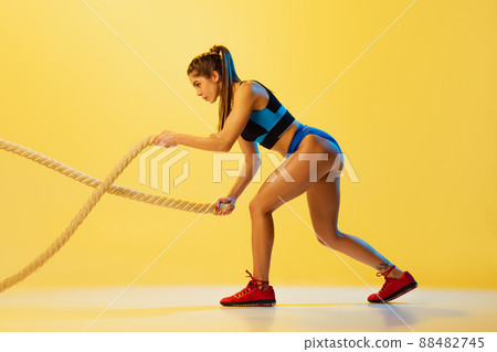 Portrait of young sportive girl training with sports ropes isolated on yellow studio background. Sport, action, fitness, youth and health concept. 88482745