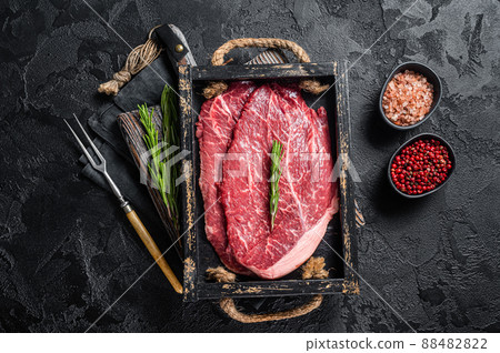 Marbled beef steak, raw meat with spices in wooden tray. Black background. Top view 88482822