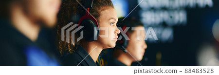 Side view of a focused mixed race girl, female cybersport gamer wearing headphones playing online video games, participating in eSport tournament Side view of a focused mixed race girl, female cybersport gamer wearing headphones playing online video games, participating in eSport tournament 88483528