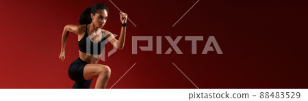 Higher and higher. Full length of young athlete woman in sports clothing jumping against red background 88483529