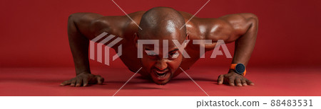 Strong african man in sports clothing doing push-ups isolated over red background Strong african man in sports clothing doing push-ups isolated over red background 88483531
