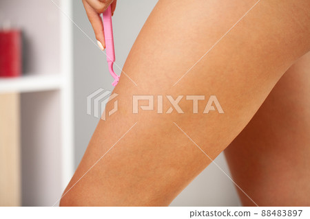 Young woman shaving legs with a razor blade in the bathroom Young woman shaving legs with a razor blade in the bathroom 88483897