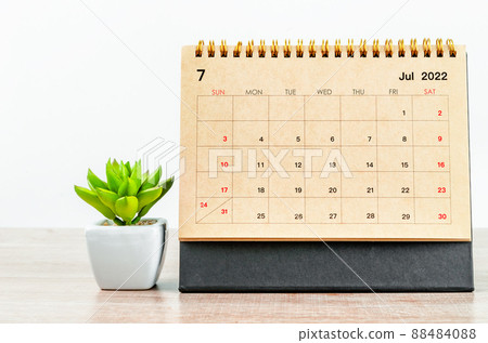 July 2022 desk calendar with plant on wooden table. 88484088