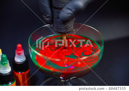 Tattoo artist dips tattoo machine in red and green ink 88487335