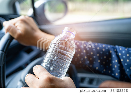 Asian woman driver holding bottle for drink water while driving a car. Plastic hot water bottle cause fire. Asian woman driver holding bottle for drink water while driving a car. Plastic hot water bottle cause fire. 88488258