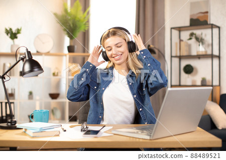 blonde woman dressed in casual jeans shirt, listening musing with headphones and dancing 88489521