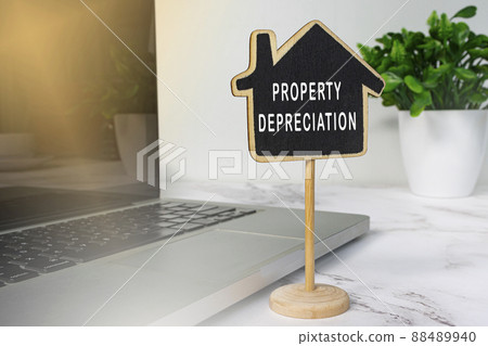 Property depreciation text on wooden house model with notebook on white desk. 88489940