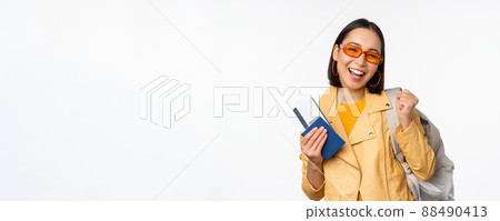 Happy asian girl going on vacation, holding passport and flight tickets, backpack on shoulder. Young woman tourist travelling abroad, standing over white background 88490413