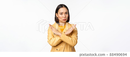 Stop gesture. Serious asian woman making arm cross, prohibit smth, rejecting, dislike and disapprove action, standing over white background Stop gesture. Serious asian woman making arm cross, prohibit smth, rejecting, dislike and disapprove action, standing over white background 88490694