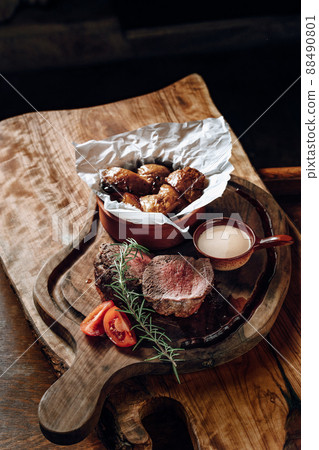 Juicy delicious steak with sauce baked potatoes on a wooden surface Juicy delicious steak with sauce baked potatoes on a wooden surface 88490801