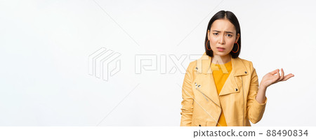 Image of frustrated korean woman, shrugging shoulders and raising hand, looking puzzled, cant understand smth, standing over white background 88490834