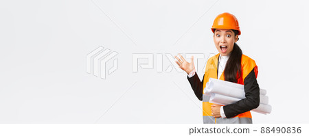 Impressed and fascinated asian female engineer, lead architect at construction area, pointing behind at something awesome, carry blueprint of project, wearing safety helmet and reflective jacket Impressed and fascinated asian female engineer, lead architect at construction area, pointing behind at something awesome, carry blueprint of project, wearing safety helmet and reflective jacket 88490836