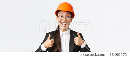 Excited happy female asian engineer, construction manager in safety helmet and business suit showing thumbs-up in rejoice, approve very good work, praise well done job, white background Excited happy female asian engineer, construction manager in safety helmet and business suit showing thumbs-up in rejoice, approve very good work, praise well done job, white background 88490973