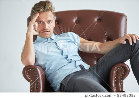 Portrait of a stylish intelligent man, small unshaven, charismatic, blue shirt, sitting on a brown leather chair, dialog, negotiation, short sleeve, brutal, hairstyle, emotions, energy, interest Portrait of a stylish intelligent man, small unshaven, charismatic, blue shirt, sitting on a brown leather chair, dialog, negotiation, short sleeve, brutal, hairstyle, emotions, energy, interest 88492082
