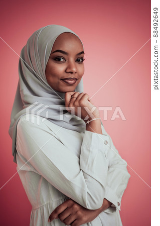 Portrait of young modern muslim afro beauty wearing traditional islamic clothes on plastic pink background. Selective focus  88492649