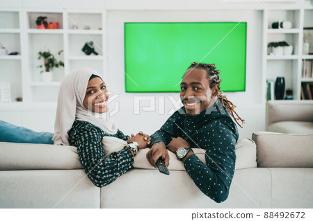 African Couple Sitting On Sofa Watching TV Together Chroma Green Screen Woman Wearing Islamic Hijab Clothes African Couple Sitting On Sofa Watching TV Together Chroma Green Screen Woman Wearing Islamic Hijab Clothes 88492672