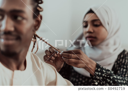 A young Muslim couple has a romantic time at home while the woman makes the hairstyle for her husband female wearing traditional Sudan Islamic hijab clothes. A young Muslim couple has a romantic time at home while the woman makes the hairstyle for her husband female wearing traditional Sudan Islamic hijab clothes. 88492719