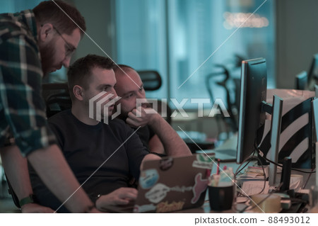 A photo of three men staring intently at a computer while sitting in a modern office. Selective focus  88493012